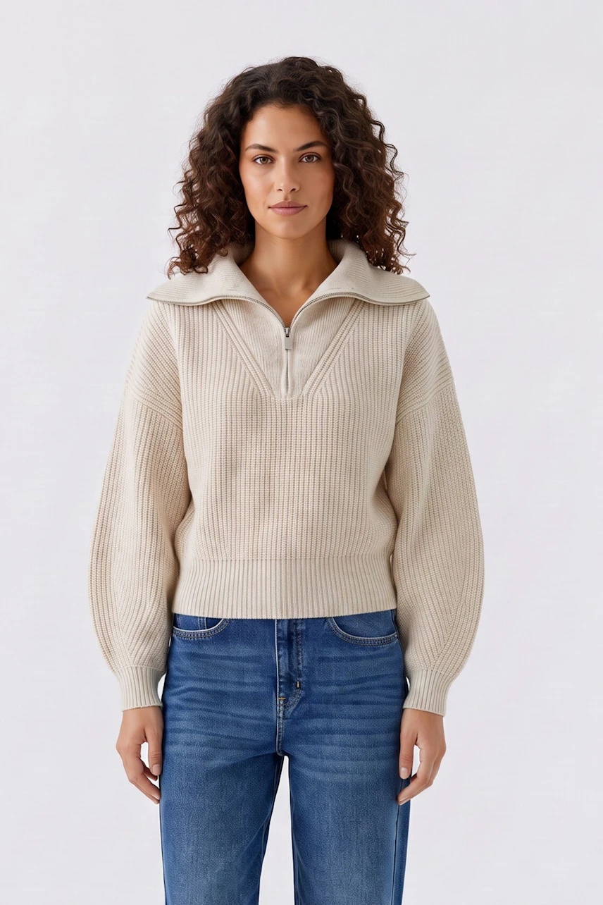Damen-Pullover: Frau im beigen Strickpullover mit Reißverschluss und lockigem Haar, kombiniert mit Jeans.