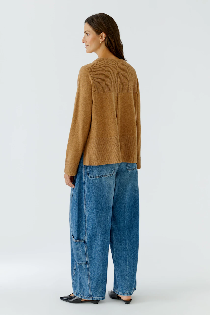 Lässiger Damen-Pullover: Frau im braunen Pullover und blauer Jeans, seitlich stehend.