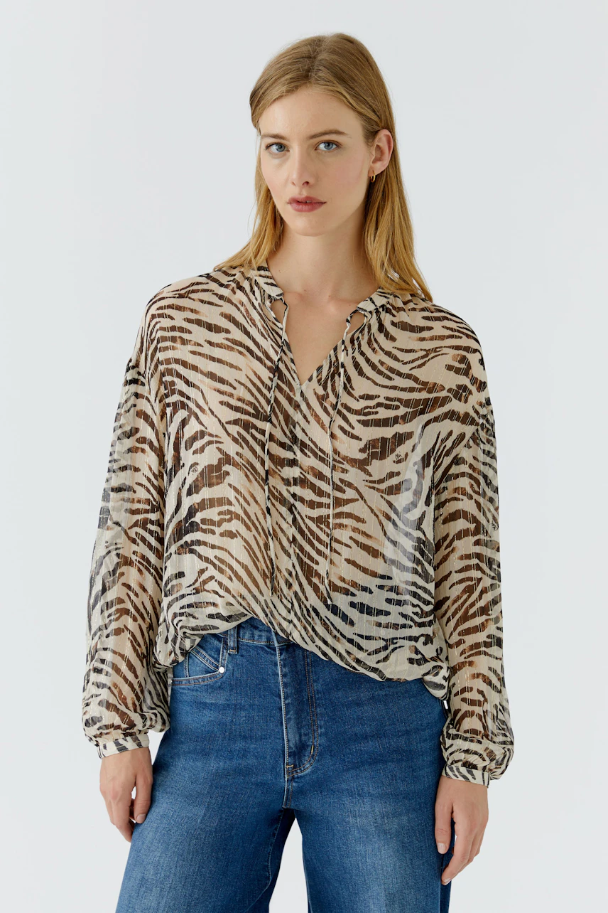 Lässige Damen-Bluse: Frau in gemusterter Bluse mit Tigerstreifen und blauer Jeans, schaut direkt in die Kamera.