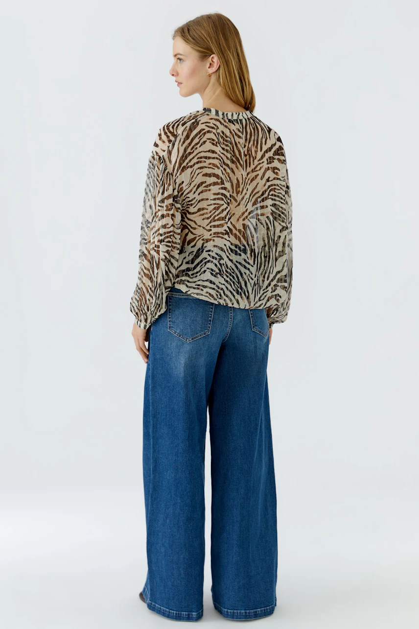 Damen-Bluse: Frau in weiter Bluse mit Zebramuster und blauer Jeans, von hinten gesehen.