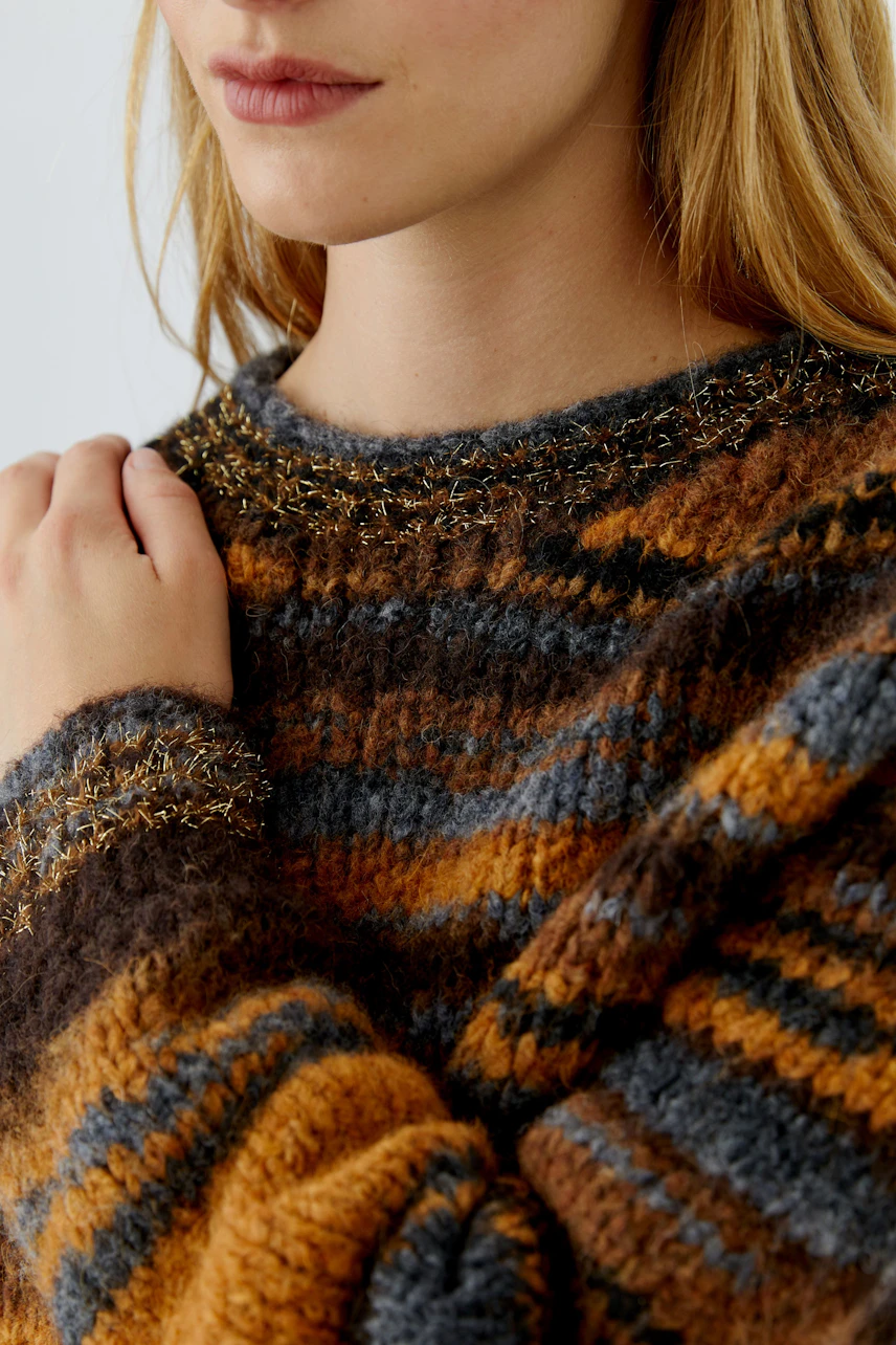 Frau im gestreiften Pullover in warmen Tönen, Hand am Kragen, lässiger Look.
