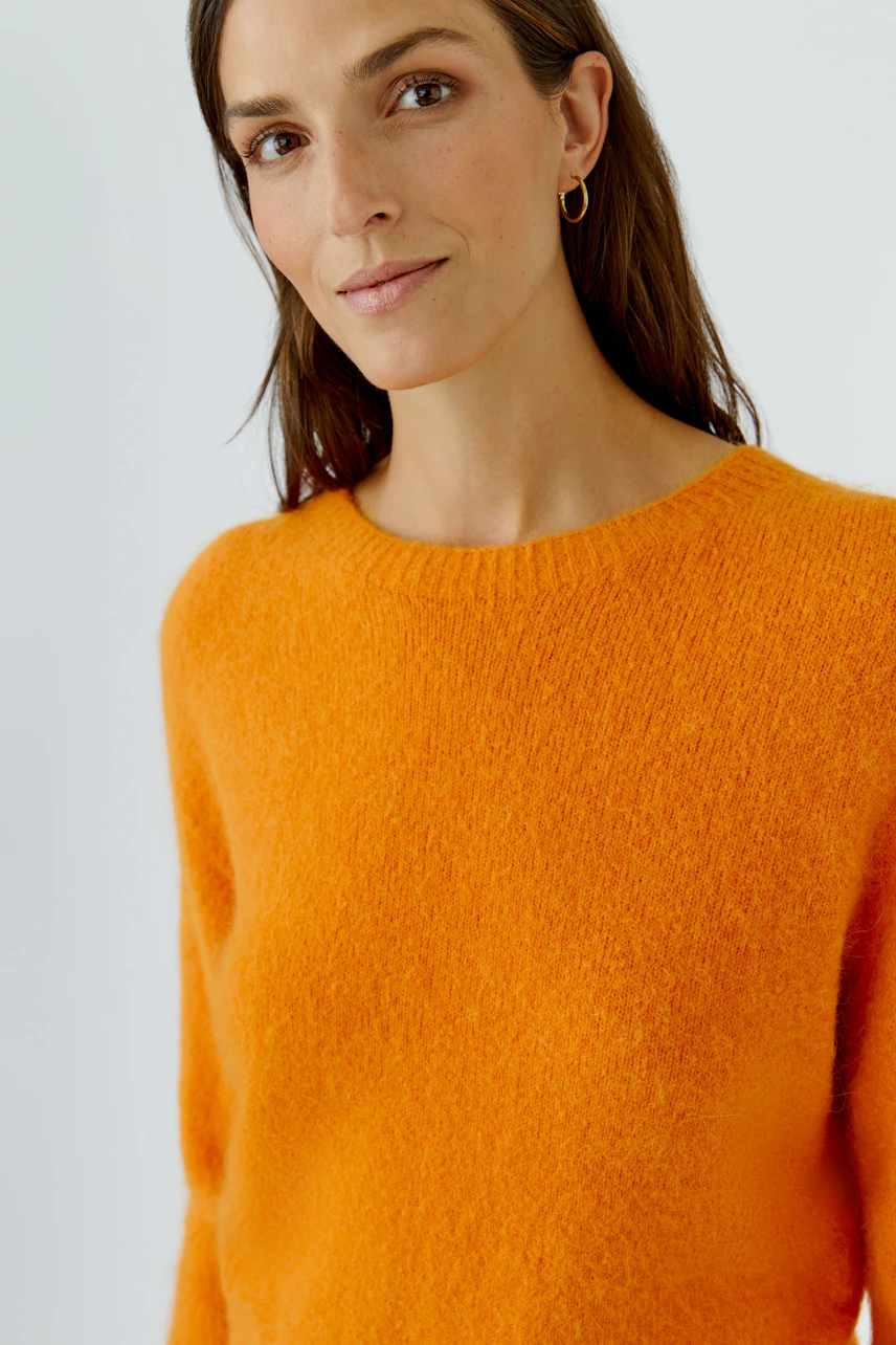 Frau im leuchtend orangefarbenen Pullover, schlichtes Design, lässiger Look.