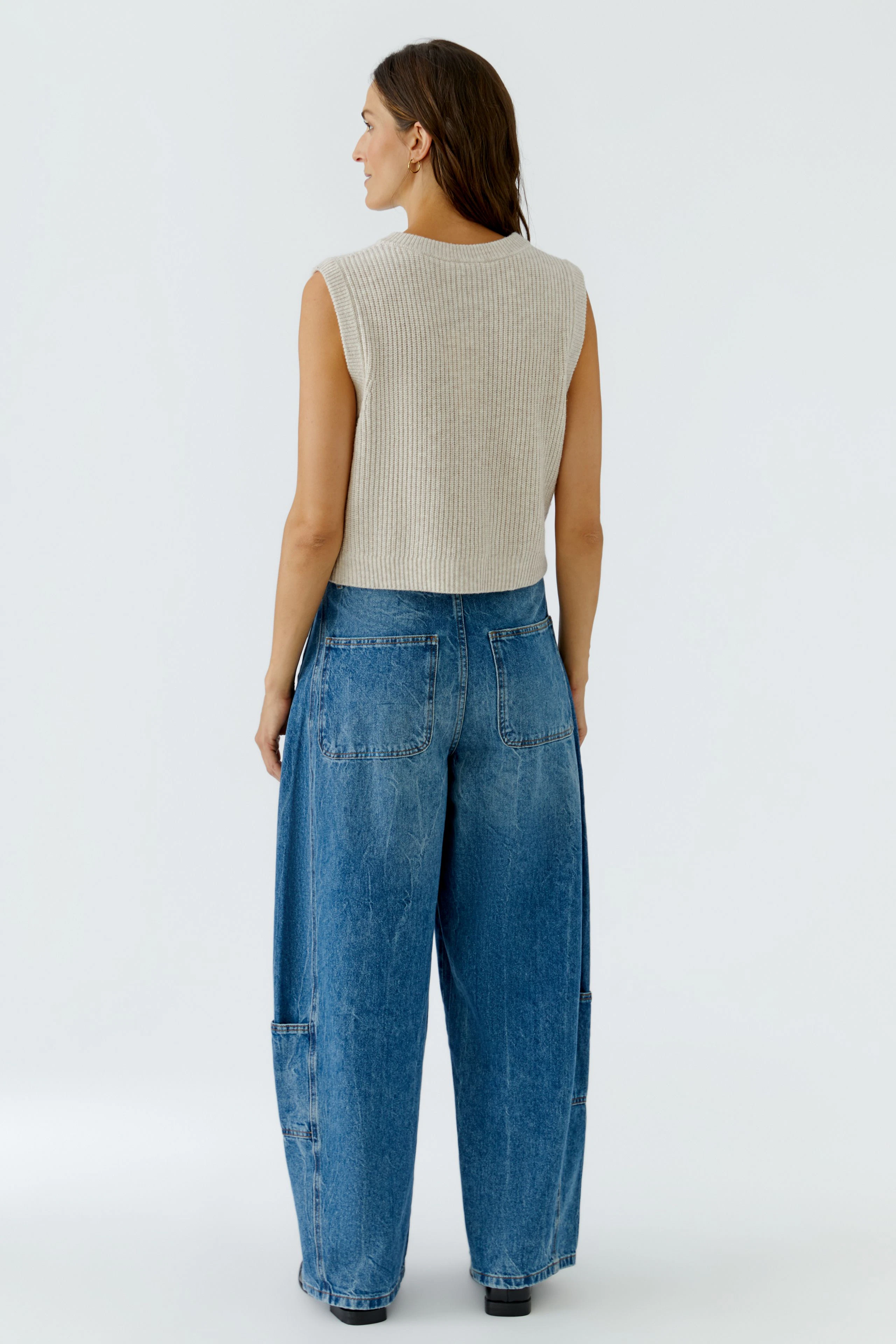 Casual knit vest: Woman in beige sleeveless knit vest and wide blue jeans, viewed from the back.