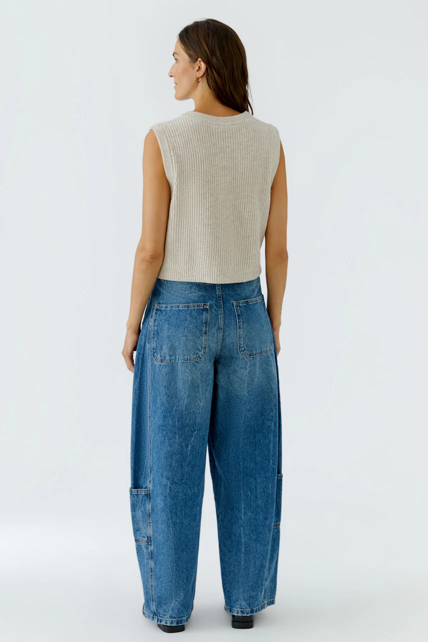 Strickweste: Frau in beiger Strickweste und blauer Jeans von hinten, lässiger Look.