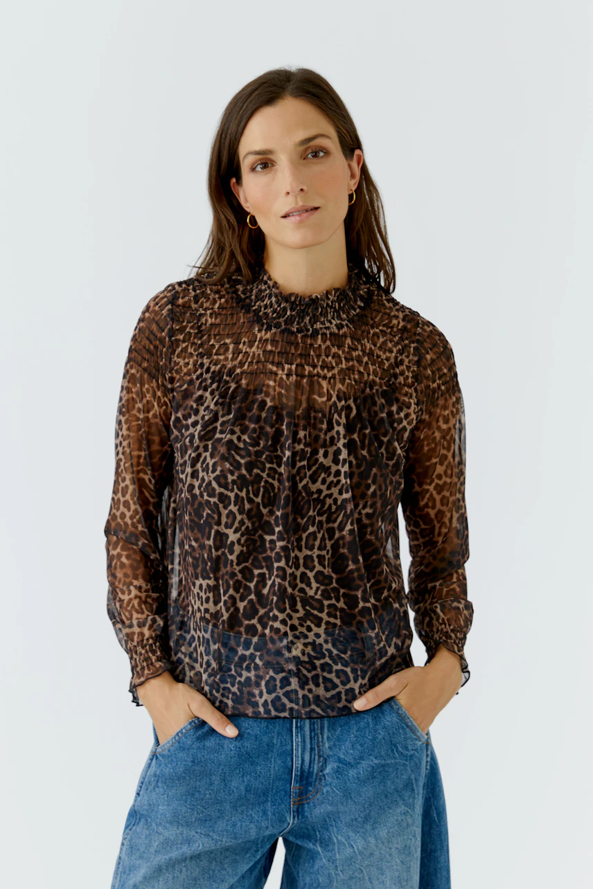 Woman in leopard print long-sleeve shirt, hands in pockets, wearing blue jeans, looking confidently.