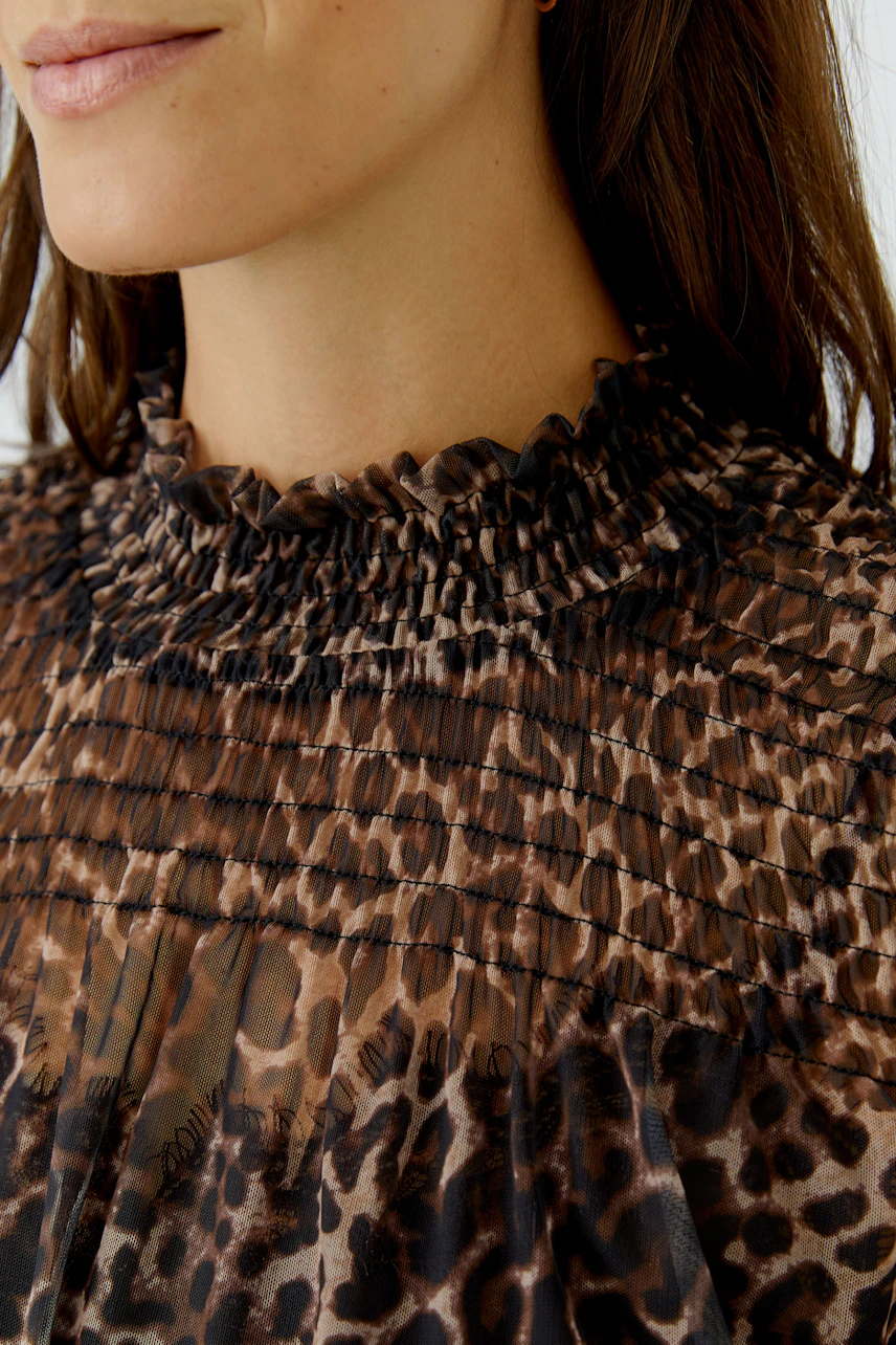 Woman in leopard print long-sleeve shirt with ruffled collar, showcasing casual style.