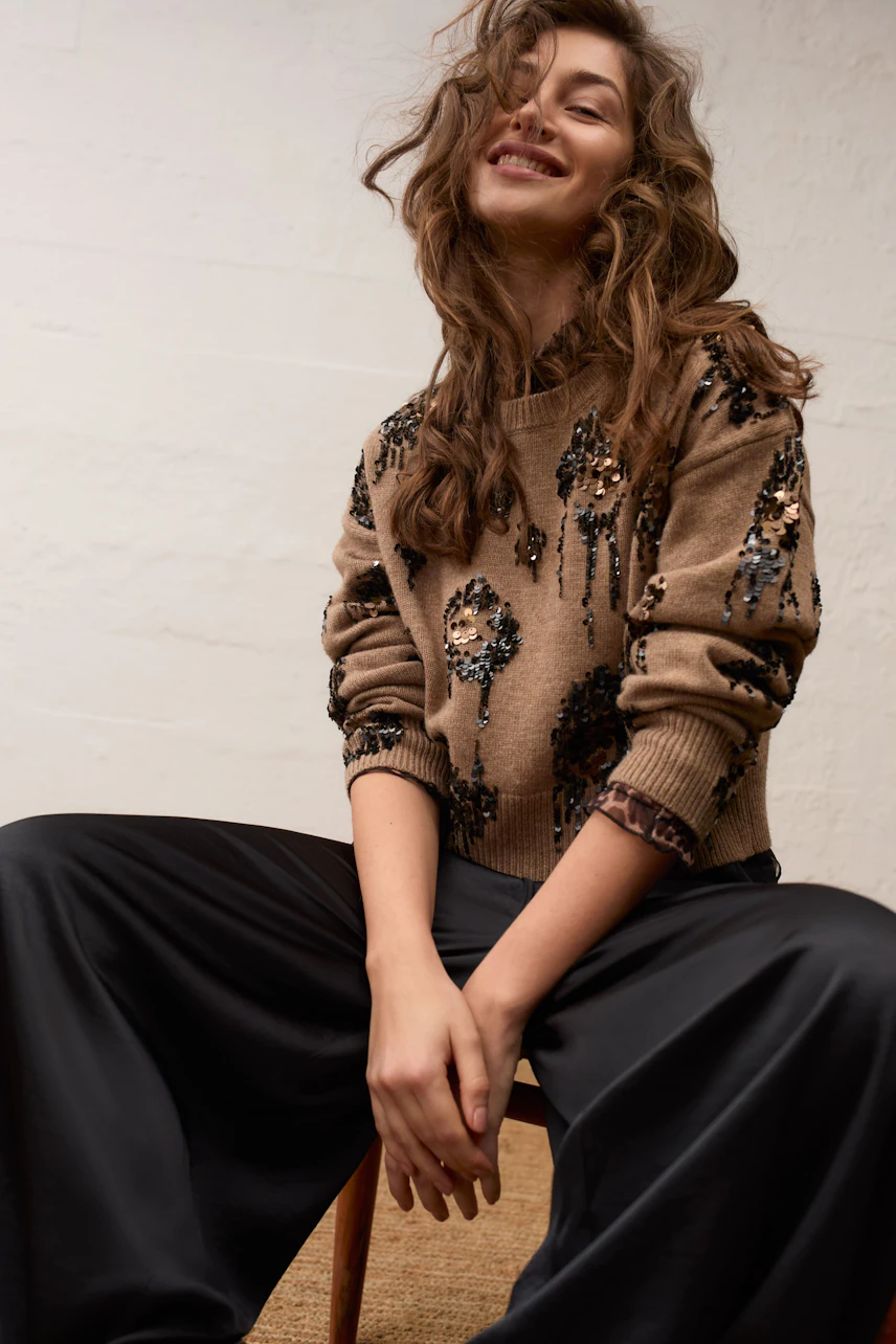 Casual long-sleeve shirt: Woman in a patterned pullover with relaxed black pants, smiling confidently.