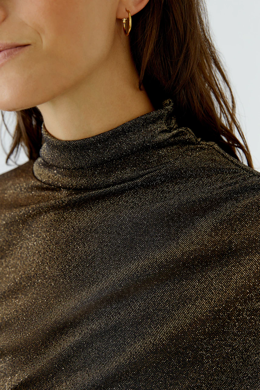 Woman in a shimmering long-sleeve shirt with a high collar, showcasing a chic and modern style.