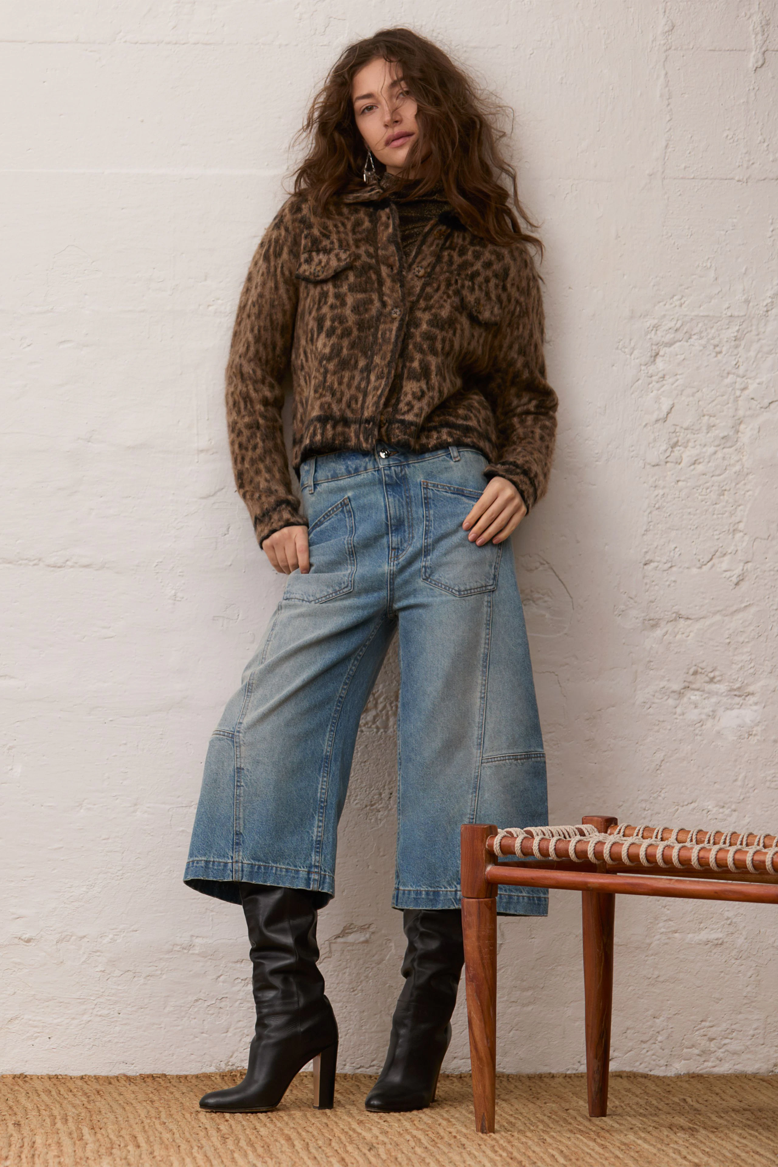 Casual long-sleeve shirt: Woman in leopard print shirt, wide jeans, and black boots stands confidently.