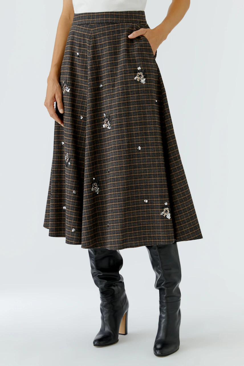 Midirock: Frau im karierten Midirock mit floralen Details und schwarzen Stiefeln.